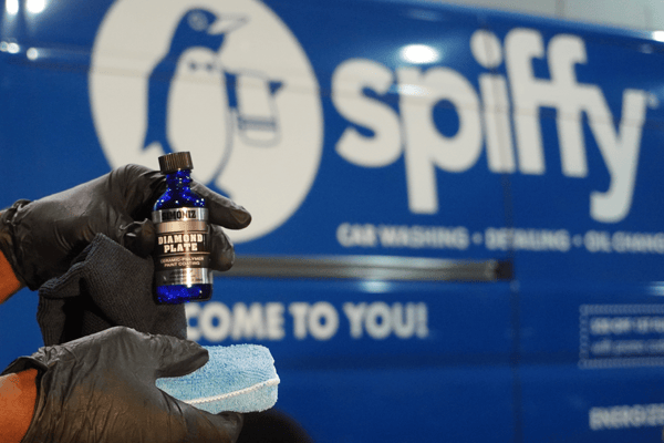 Spiffy technician showcases our ceramic coating product of choice: Simoniz Diamond Plate, in front of a Spiffy van.